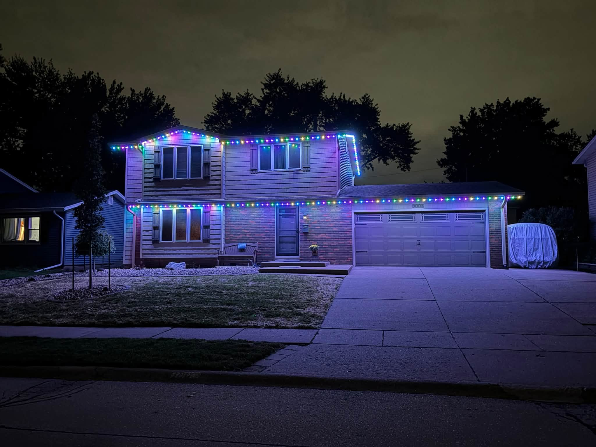Two-story home with colorful multicolor LED holiday lights along roofline
